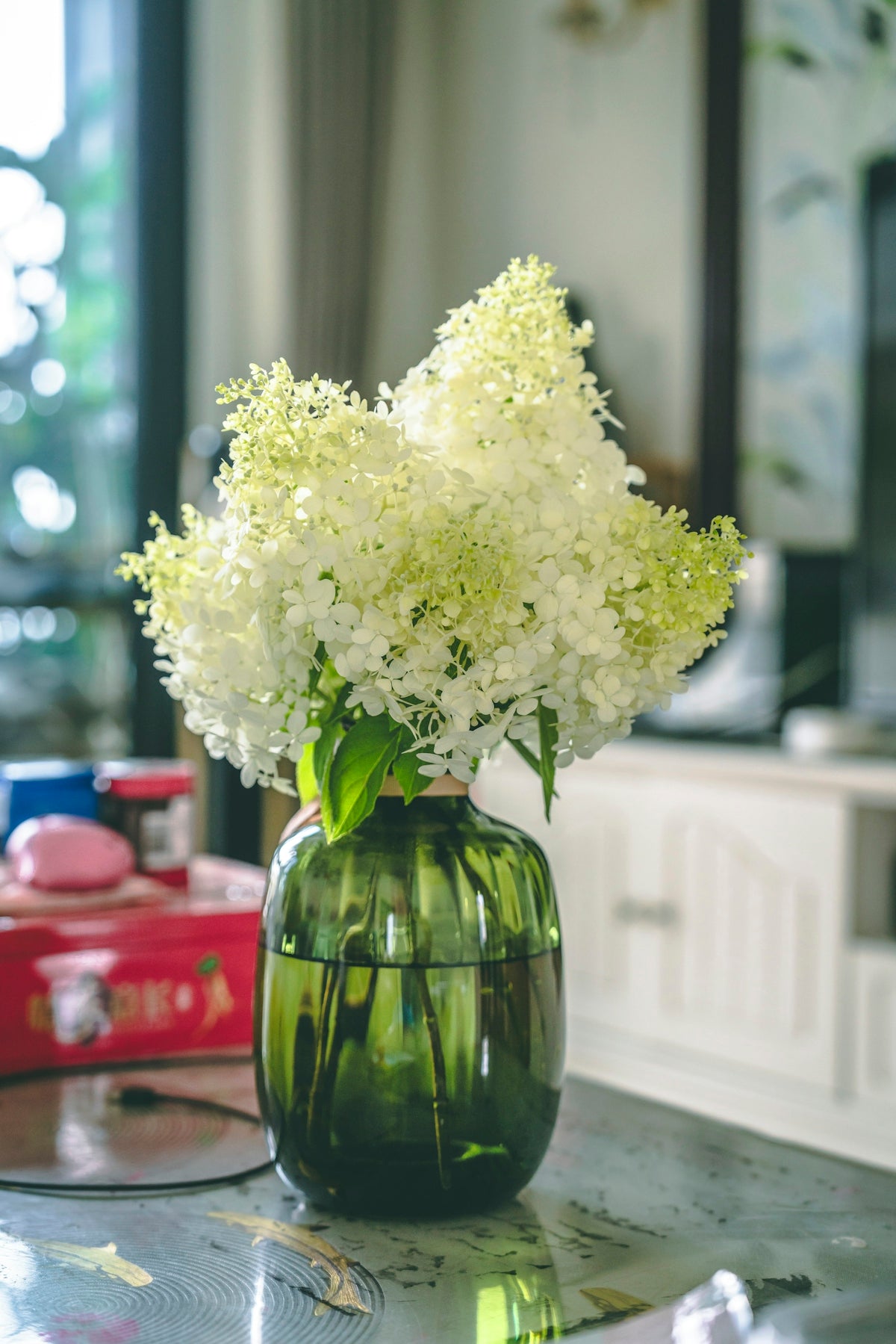 White flowers bloom from a green glass vase.