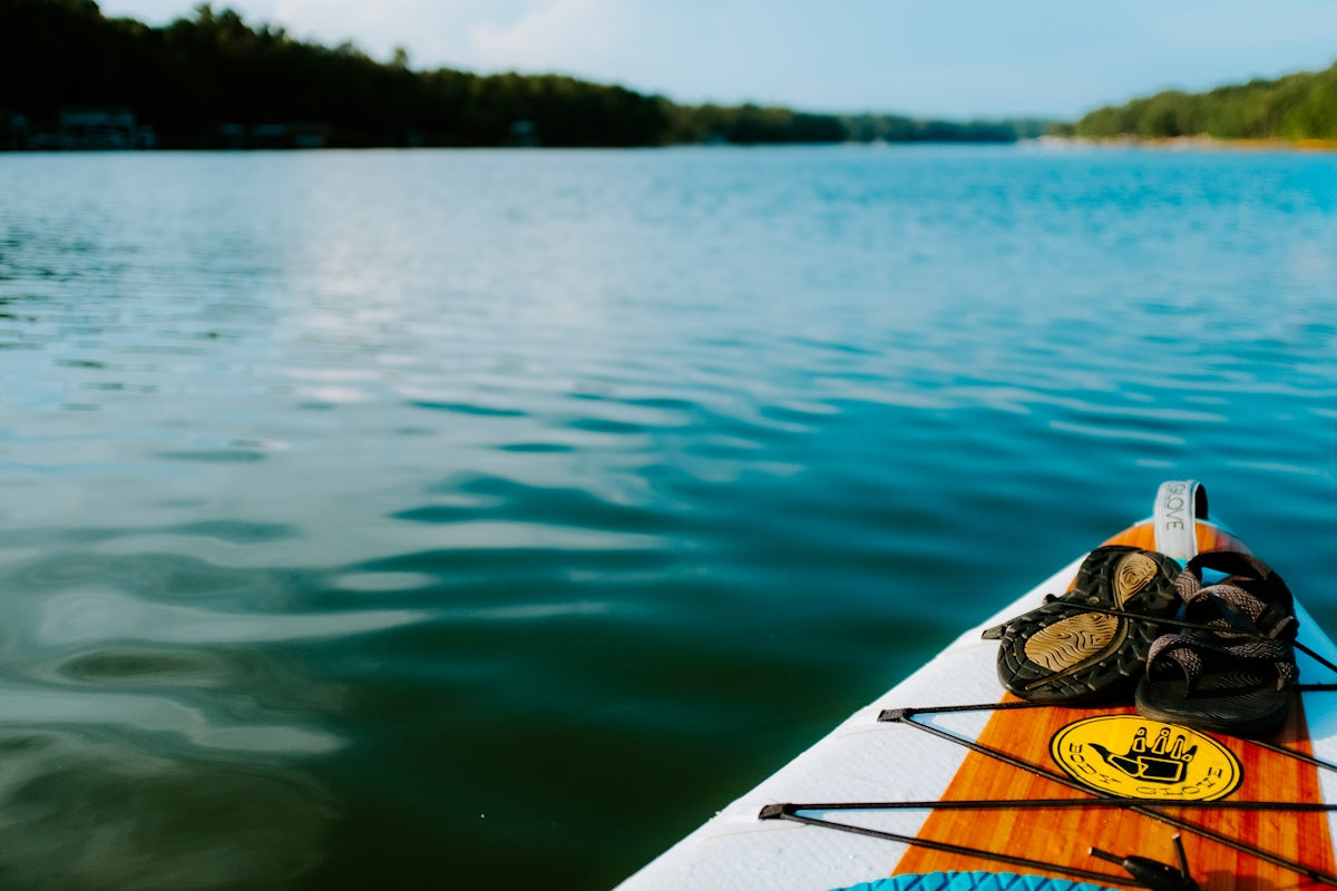 Shoes rest on a paddleboard on a lake.
