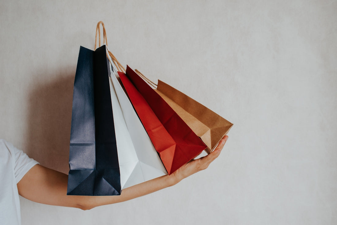 Hand holding colorful shopping bags against a light wall.