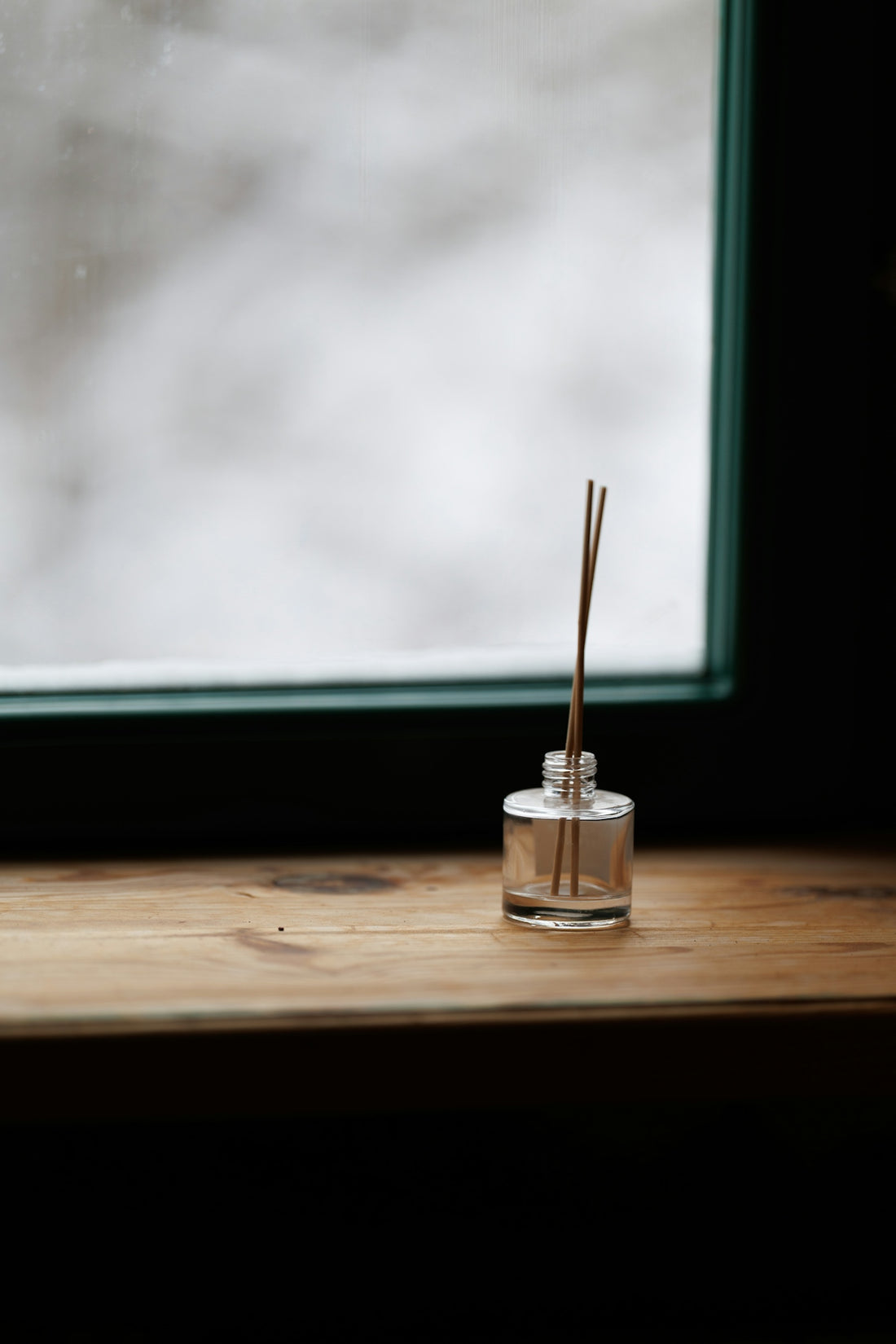 Reed diffuser bottle on a wooden surface by window.